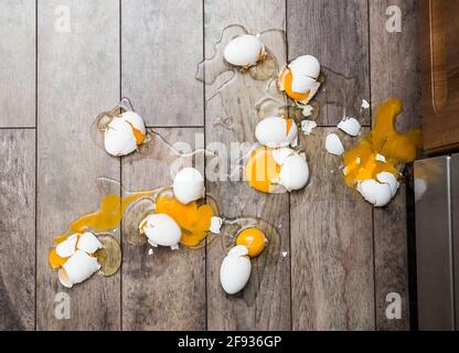 Viele zerbrochene Eier auf braunem Boden. Missgeschick-Konzept. Stockfoto