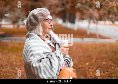 Eine Dame in einer warmen Wolldecke hält ein Papier tasse heißen Tee oder Kaffee trinken, während Sie die genießen Schöne Aussicht in der Herbstsaison Stockfoto