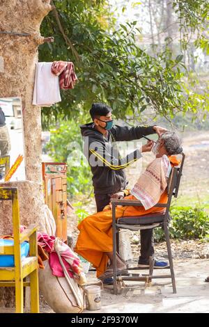 HARIDWAR, UTTARAKHAND, INDIEN - FEBRUAR 2021 : ein nicht identifizierter Barber auf der Straße von Haridwar in der Nähe von Har KI Pauri Ghat den Kunden rasieren. Stockfoto