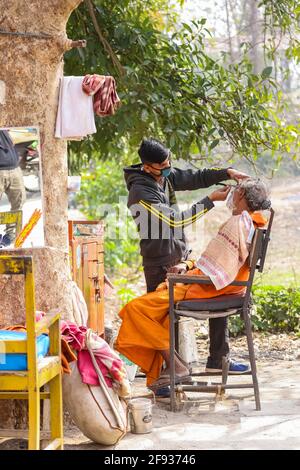 HARIDWAR, UTTARAKHAND, INDIEN - FEBRUAR 2021 : ein nicht identifizierter Barber auf der Straße von Haridwar in der Nähe von Har KI Pauri Ghat den Kunden rasieren. Stockfoto
