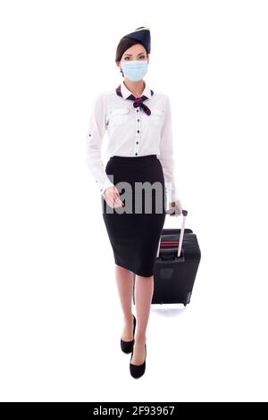 Junge Stewardess in medizinischer Maske, die mit einem isolierten Koffer unterwegs ist Weißer Hintergrund Stockfoto