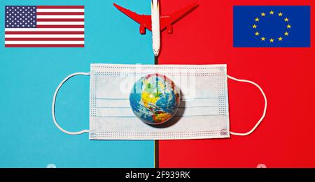 Draufsicht des Flugzeugmodells mit Gesichtsmaske und Globus auf blauem und rotem Hintergrund. Flaggen der Vereinigten Staaten und der Europäischen Union. Konzept für sichere internationale Reisen. Stockfoto