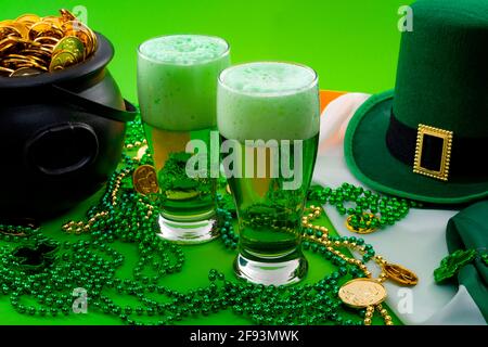 Das Glück des irischen Meme und Happy St. Patricks Day-Konzeptes mit zwei Gläsern gefärbtem Bier, Kobold-Hut, Perlenkette und einem Topf mit Goldmünzen Stockfoto