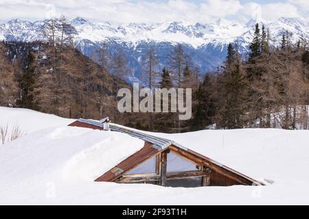 Malerische Szene mit Holzhütte bedeckt mit tiefem Schnee mit Panoramablick auf die alpen Berge. Zauberhafte Winterlandschaft. Dach der Hütte unter dem snowdri Stockfoto