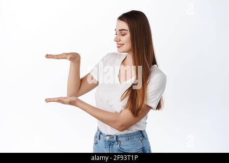 Schöne junge Frau mit gesund hydratisiert Haut, hält leeren Raum in Box Geste, zeigt Copyspace in ihren Händen, stehend über weißem Hintergrund Stockfoto