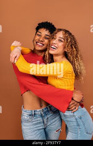 Stock Foto von fröhlichen afro Frauen umarmt einander im Studio vor braunem Hintergrund geschossen. Stockfoto