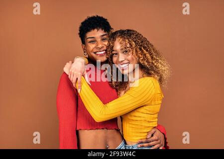 Stock Foto von fröhlichen afro Frauen umarmt einander im Studio vor braunem Hintergrund geschossen. Stockfoto