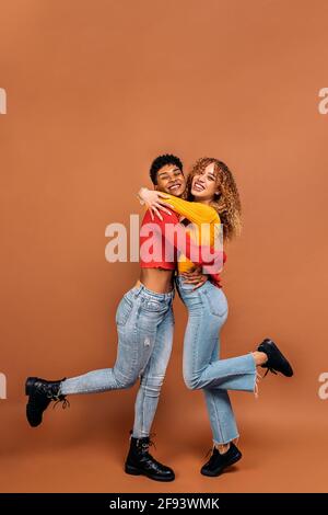 Stock Foto von fröhlichen afro Frauen umarmt einander im Studio vor braunem Hintergrund geschossen. Stockfoto