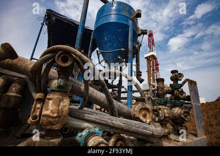 Verrostete Schlammpumpmaschine links. Ölbohrgerät (Derrick) rechts.Öllagerstätte Zhaikmunai, Kasachstan. Stockfoto