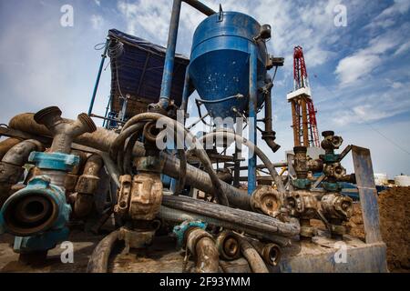 Verrostete Schlammpumpmaschine links. Ölbohrgerät (Derrick) rechts.Öllagerstätte Zhaikmunai, Kasachstan. Stockfoto