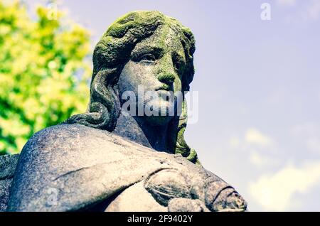 Verwitterte Statue eines Engels mit rissigem, schmutzigem Gesicht (Mit einer Spinne) Bedeckt mit Moos auf dem alten Friedhof - kreuzverarbeites Bild Stockfoto