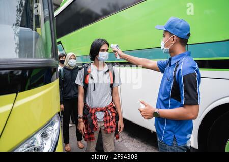 Eine Buscrew in blauen Uniformen und einem Hut mit Eine Thermopistole inspiziert den männlichen Beifahrer in der Maske Stockfoto