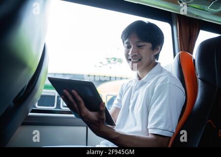 asiatischer junger Mann lächelt, während er ein Pad benutzt, während er sitzt Stockfoto