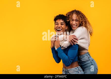 Stock Foto von fröhlichen afro Frauen umarmt einander im Studio vor gelbem Hintergrund geschossen. Stockfoto