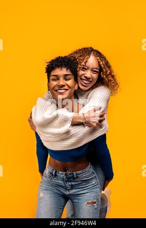 Stock Foto von fröhlichen afro Frauen umarmt einander im Studio vor gelbem Hintergrund geschossen. Stockfoto