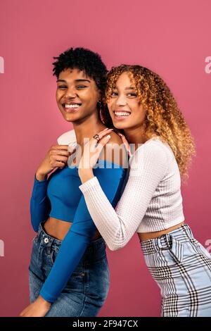 Stock Foto von fröhlichen afro Frauen umarmt einander im Studio vor rosa Hintergrund geschossen. Stockfoto