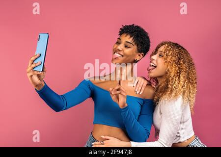 Stock Foto von fröhlichen afro Frauen posieren, während Selfie im Studio vor rosa Hintergrund aufgenommen. Stockfoto