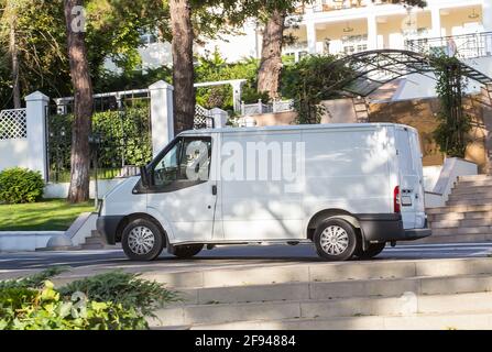 Der weiße Lieferwagen steht im Schatten der Bäume auf dem Bürgersteig am Eingang des Sanatoriums, umgeben von einem weißen Zaun. Stockfoto