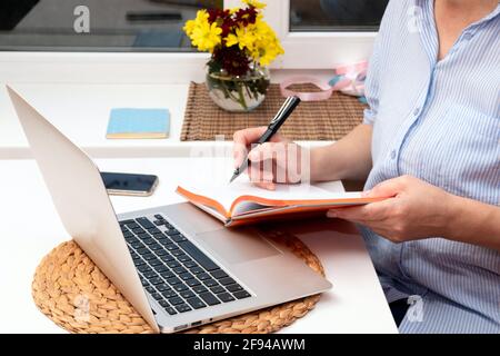 Eine Frau macht Notizen in einem Notizbuch, während sie an einem Laptop sitzt. Selektiver Fokus. Stockfoto