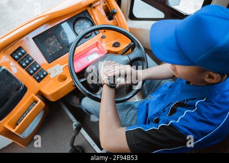 Nahaufnahme eines männlichen Fahrers in Uniform, der sich ansieht Seine Uhr, während er das Rad hält Stockfoto