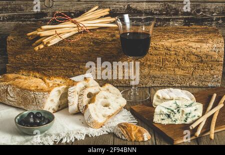 Knuspriges französisches Weißbrot, Käse und Rotwein auf rustikalem Holztisch Stockfoto