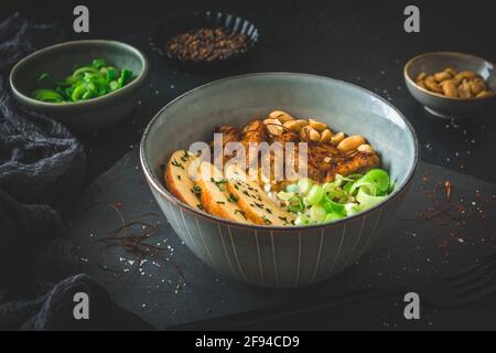 Buddha-Schüssel mit Huhn, Reis, Erdnüssen, Apfel- und Chilisauce auf dunklem Hintergrund Stockfoto