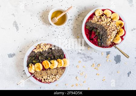 Gesundes Frühstück. Smoothie-Schalen mit Heidelbeeren, Banane, Haferflocken, Chiasamen, Quinoa, Kürbiskerne und Honig. Draufsicht. Stockfoto