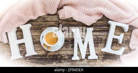 Das Wort Home in weißen Buchstaben, die O durch eine Tasse Kaffee ersetzt, mit einem rosa Wolle Pullover, Konzept der gemütlichen Atmosphäre Stockfoto