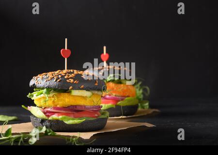 Love Konzept von zwei Vegan Burger von schwarzen Kohlebuns, Gemüse Fleischbällchen Pflanzen Fleisch auf schwarzem Hintergrund. Nahaufnahme. Stockfoto