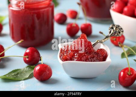Hausgemachte Süßkirschkonfitüre in einer weißen Schale und Gläser auf hellblauem Hintergrund. Stockfoto