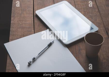 Büroarbeitsplatz mit Tablet-pc auf dem Tisch. Auf dem Tisch befindet sich ein Tablett und ein weißes Blatt Papier mit einem Stift. Für eine Design-Präsentation oder ein portf Stockfoto