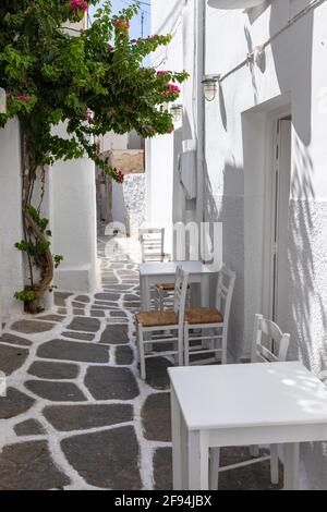 Blick auf die schmale Straße des Fischerdorfes mit lokalem Restaurant und Geschäften. Außentische für Gäste. Naoussa, Insel Paros, Griechenland. Stockfoto