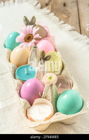 Box mit pastellfarbenen ostereiern, Kerzen in Eierschalen und Frühlingsblumenblüten als Osterdekoration Stockfoto