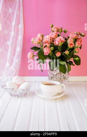 Eine Tasse Tee, Süßigkeiten und ein Strauß Rosen auf einem rosa Hintergrund. Gemütliches Zuhause. Stockfoto