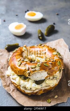Bagel-Brötchen-Sandwich mit Eiersalat auf grauem Hintergrund, vertikal Stockfoto