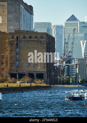 London, 2019. Dezember - Alt und Neu zusammen, das veraltete Geschoss der alten Millennium Mills Lagerhäuser und die eleganten, modernen Türme von Canary Wharf. Stockfoto