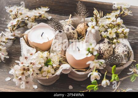 Kerzen in Eierschalen, Wachteleiern und weiß blühenden Apfelbaumbästen auf einem Holztablett als Osterdekoration Stockfoto