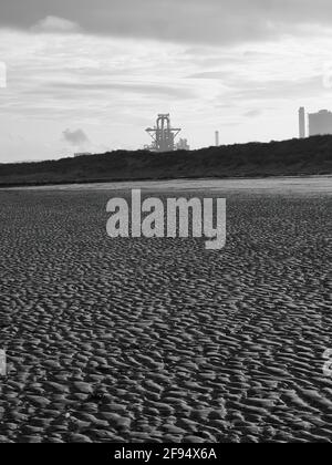 Das verlassene, verlassene Brut des Hochofens am Redcar Steelworks hinter Dünen, von einem Strand aus kompliziert strukturiertem und gewelltem Sand aus gesehen. Stockfoto