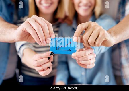 Eine Gruppe von vier jungen motivierten Menschen, die ein blaues Papier mit einer wachsenden Geschäftsgrafik halten. Stockfoto