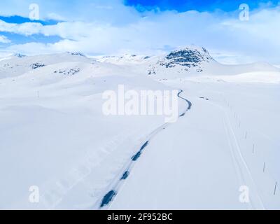 Einsame gefrorene Straße, die sich durch eine schneebedeckte Berglandschaft schlängelt. Stockfoto