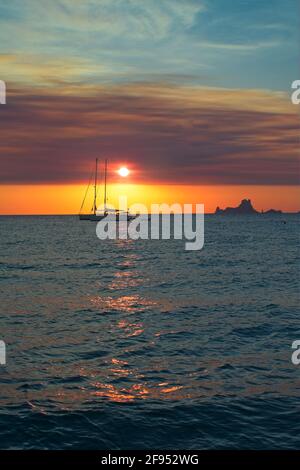Zwei Segelboote vor Anker bei Sonnenuntergang vor einem Strand auf der Insel Formentera in Spanien. Im Hintergrund die Sonne am Horizont Stockfoto