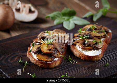 Bruschetta mit Pilzen, Frischkäse und Microgreens auf rustikalem Holzhintergrund. Stockfoto