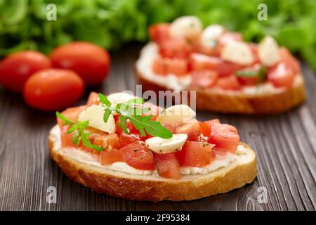Hausgemachte Bruschetta mit Tomaten und Mozzarella auf einem rustikalen Holzbrett. Stockfoto