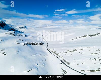 Einsame Straße, die sich durch eine schneebedeckte Berglandschaft schlängelt. Stockfoto