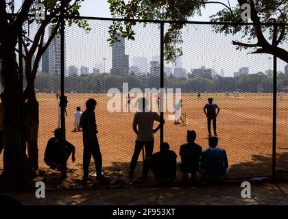 Silhouette von Teenagern, die hinter einem Zaun stehen und ein Cricket-Spiel im Shivaji Park in Mumbai-Dadar, Maharashtra, Indien, beobachten Stockfoto