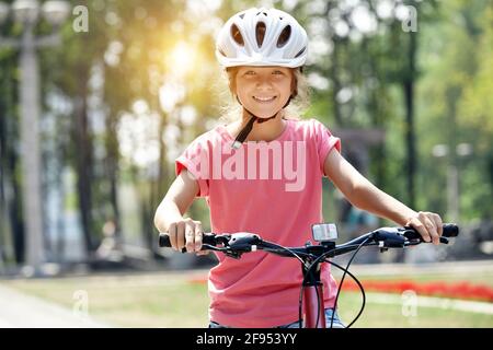 Mädchen mit Helm und Fahrrad im Stadtpark. Schaut auf die Kamera und lächelt. Stockfoto