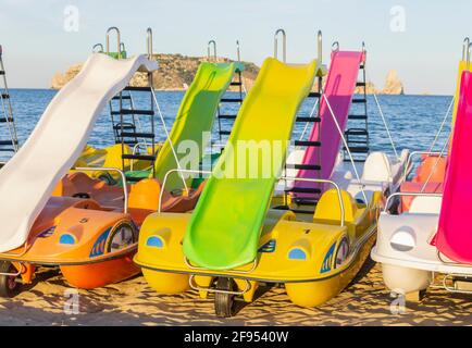 Bunte Tretboote oder Paddelboote mit Rodel am Strand.Sommerkonzept mit Tretbooten mit dem Mittelmeer im Hintergrund.Spanien. Stockfoto