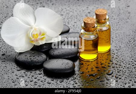 Weiße Orchidee, schwarze Steine und Ölflaschen auf hängenden Hintergrund. Stockfoto