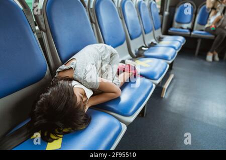 Ein kleines Mädchen schlief auf einer Bank in der ein Bus Stockfoto