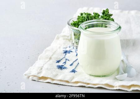 Saure Sahne oder Naturjoghurt in einem Glas mit Löffel, Gesundheit und Diät-Konzept auf hellgrauem Schiefer Hintergrund. Stockfoto